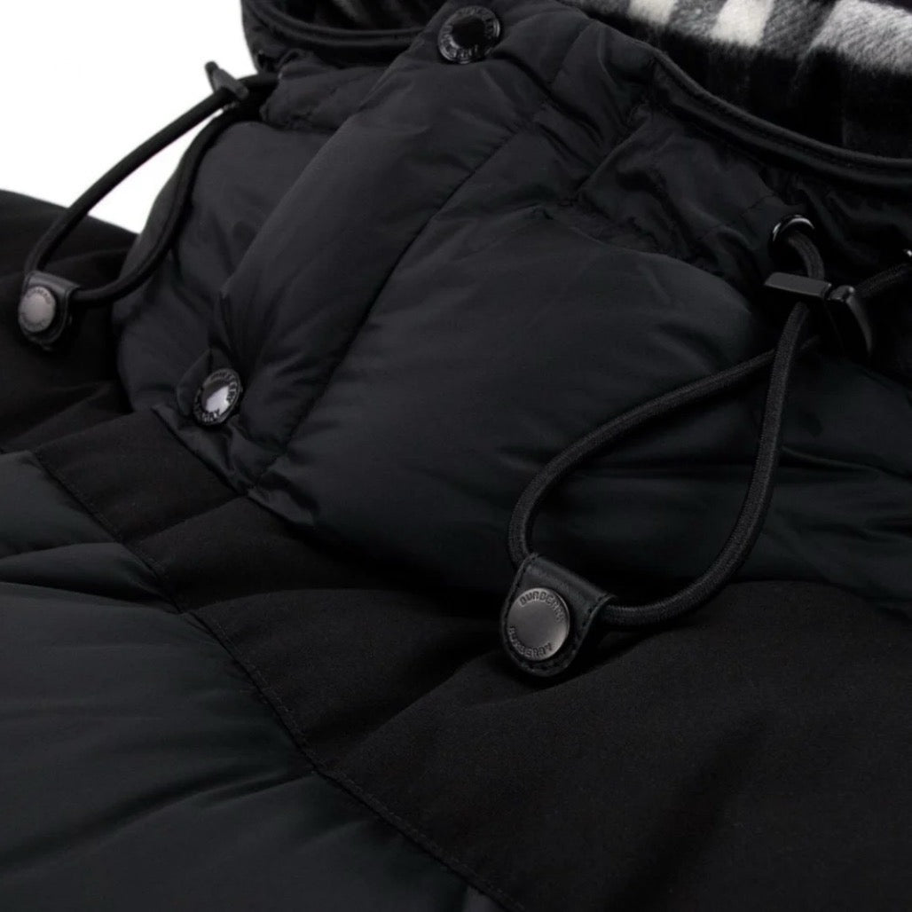Close-up of a black quilted jacket with buttons and drawstrings on a white background