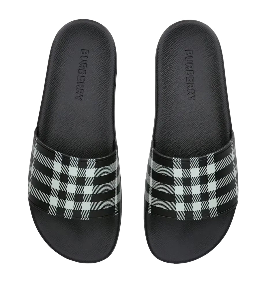 A pair of Burberry slide sandals with a black and white check pattern strap, shown from a top-down view on a light gray background.