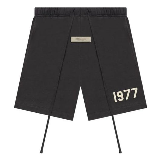 Black essentials shorts with '1977' print on a white background, long drawstrings and small essentials brand in the centre of the shorts