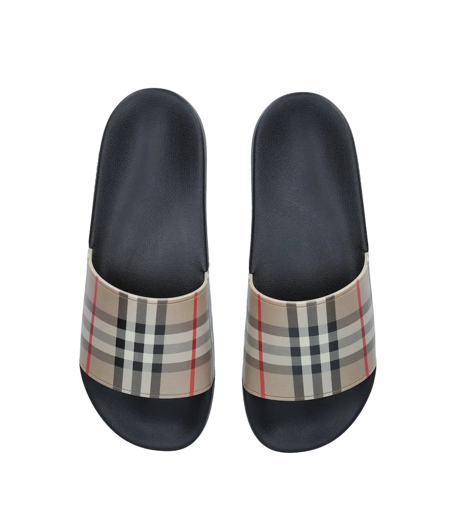 A pair of Burberry checkered slide sandals with black footbeds and a beige plaid strap featuring black, gray, and red lines, shown from a top-down view on a white background.