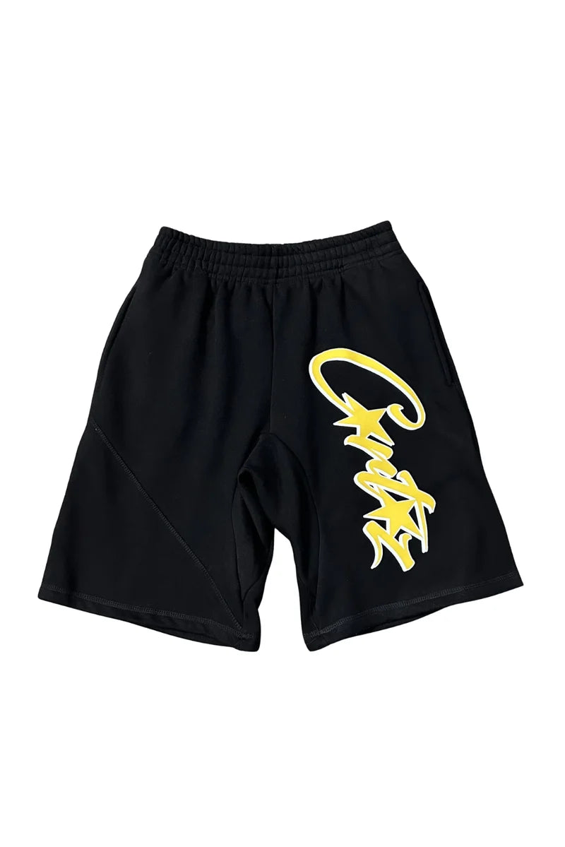 Black athletic shorts with a large yellow stylized graphic on the left leg, displayed against a solid white background.